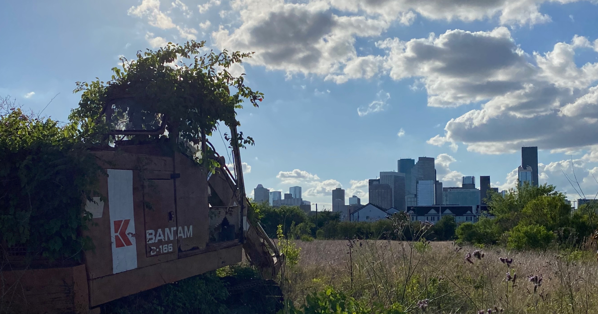 Overgrown industrial machinery with the Houston skyline in the background.